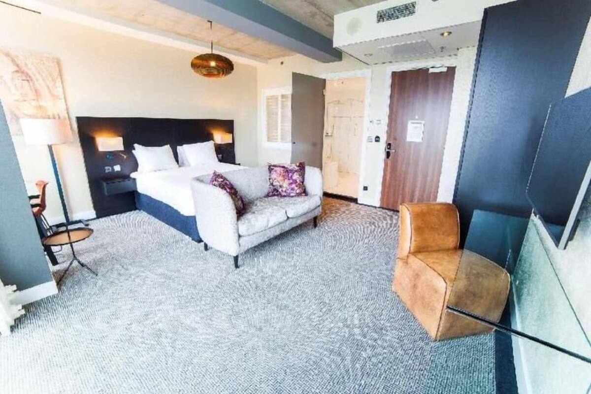 Une chambre d’hôtel avec un lit, un canapé, une chaise, une lampe et une porte.