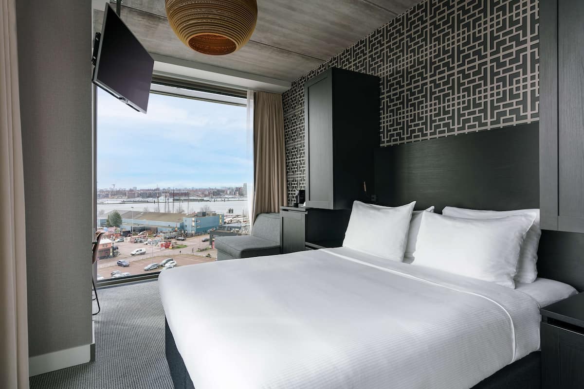 Une chambre d’hôtel avec un grand lit, un téléviseur fixé au mur et une vue sur le paysage urbain par la fenêtre.