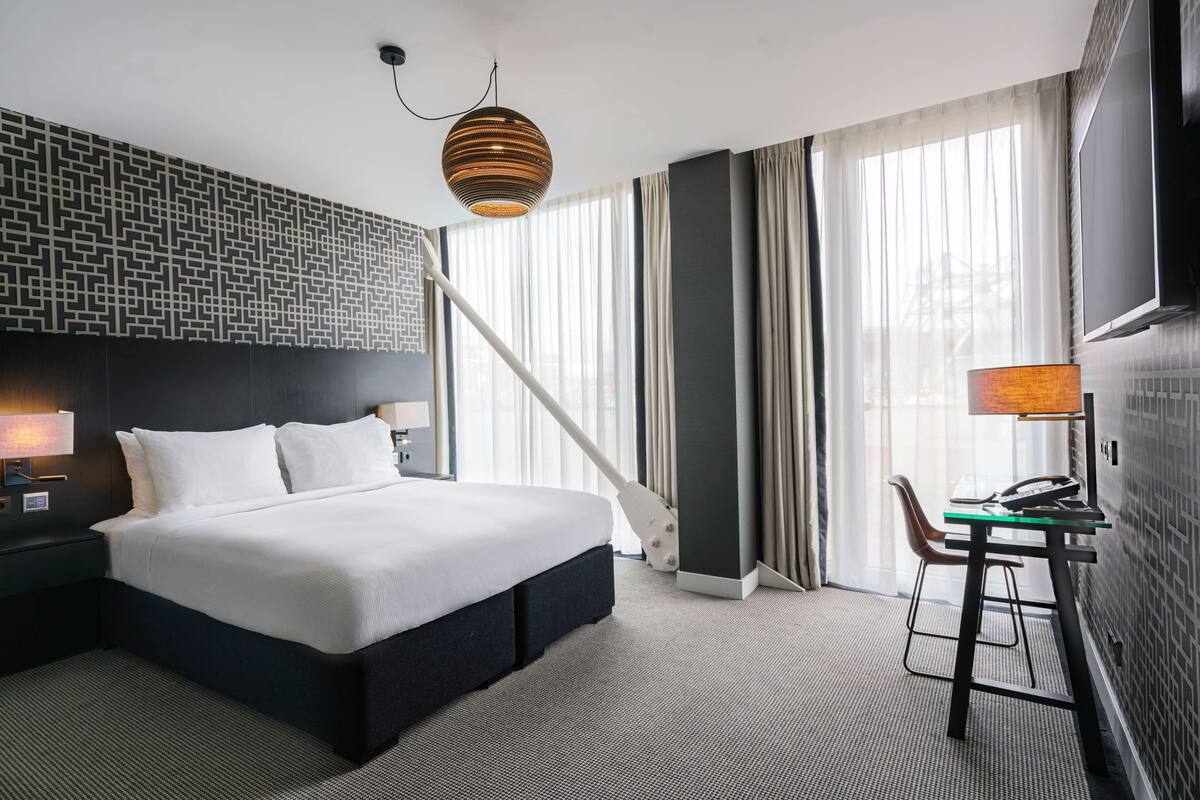 Une chambre d’hôtel moderne avec un grand lit, un bureau avec une chaise, une télévision et un mur décoré de motifs.