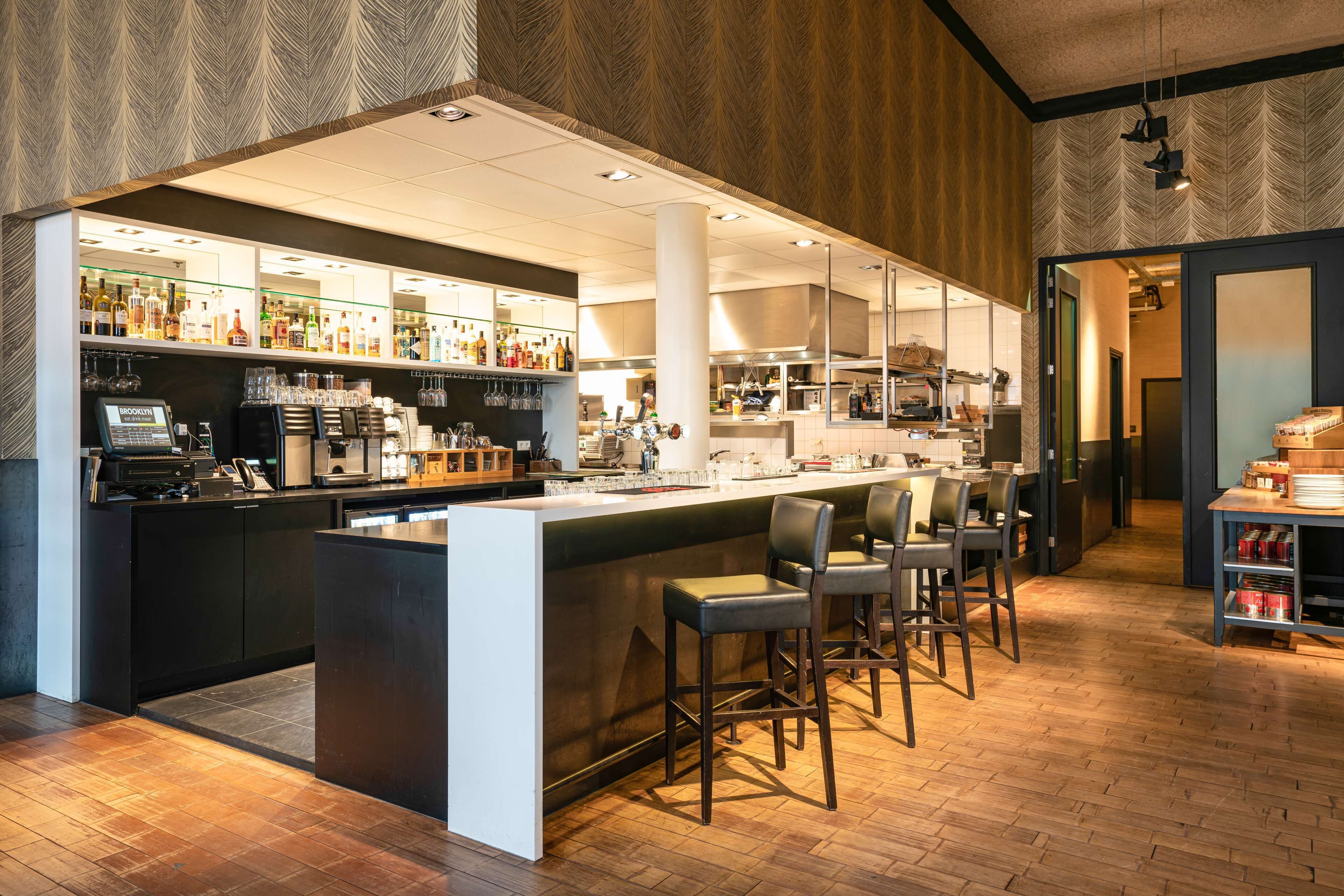 A modern bar area with a counter, stools, and a variety of bottles and glasses.