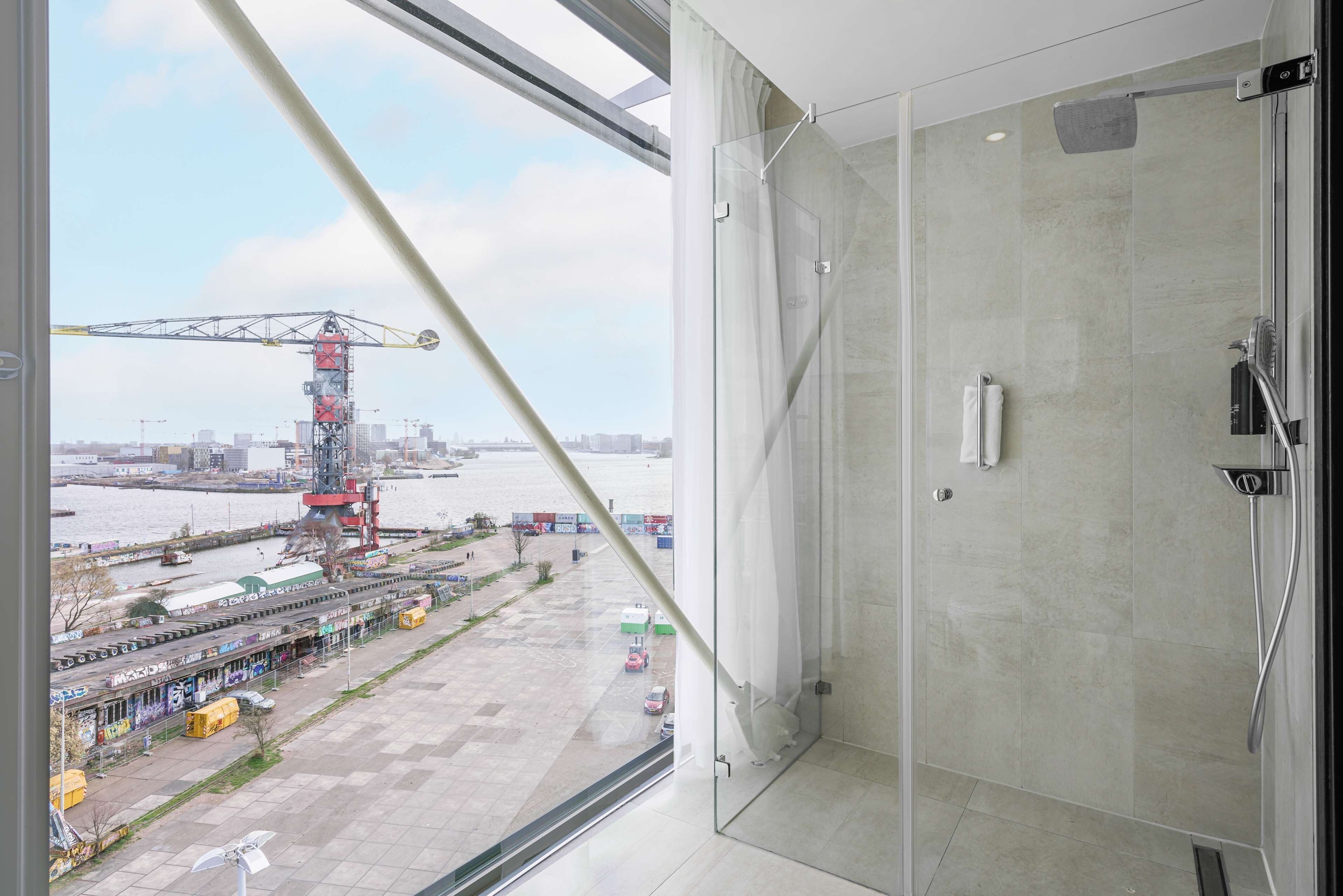 Ein modernes Badezimmer mit Duschkabine aus Glas, einem Handtuch und Blick auf eine Baustelle mit Kran und abgestellten Fahrzeugen.
