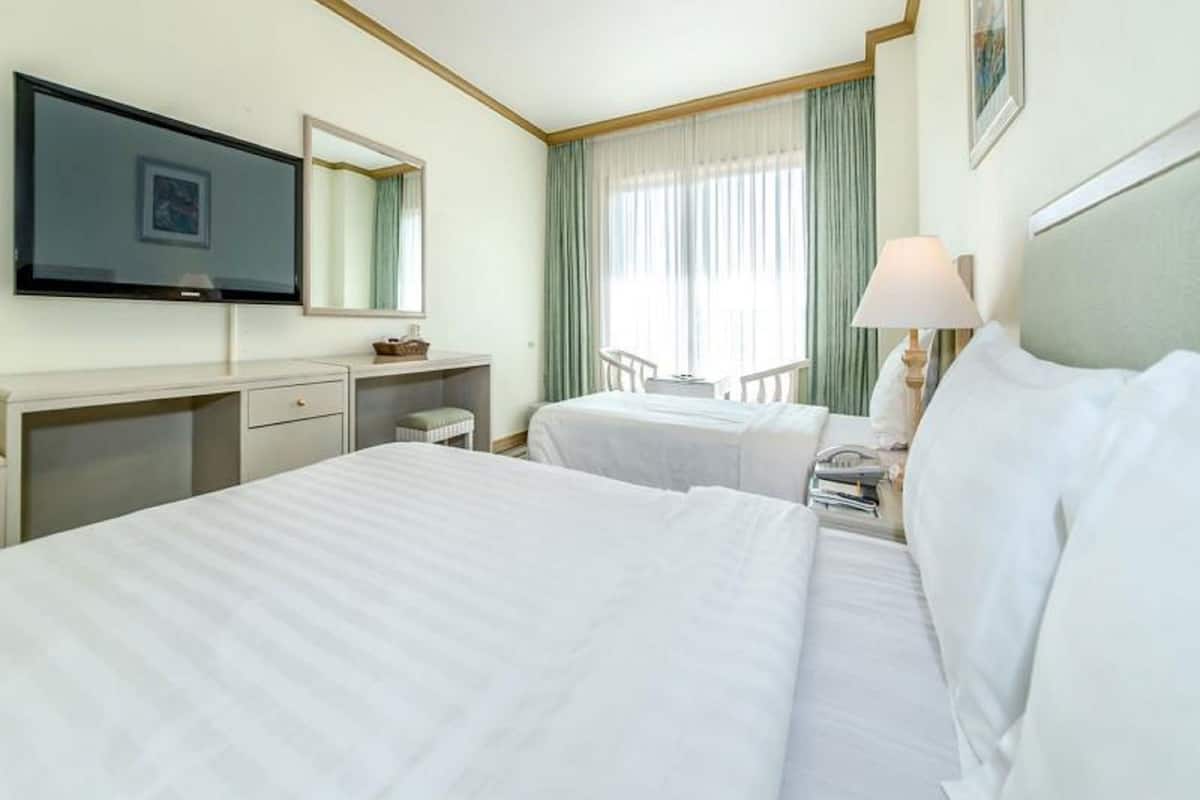 A hotel room with two beds, a desk, a chair, a TV, and a window with curtains.