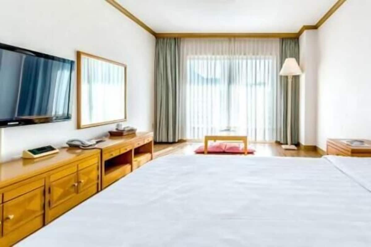 A hotel room with a large bed, wooden dresser, bedside table, lamp, and a TV on the wall.