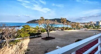 Vista de playa con palmeras, una zona arenosa y una colina al fondo.