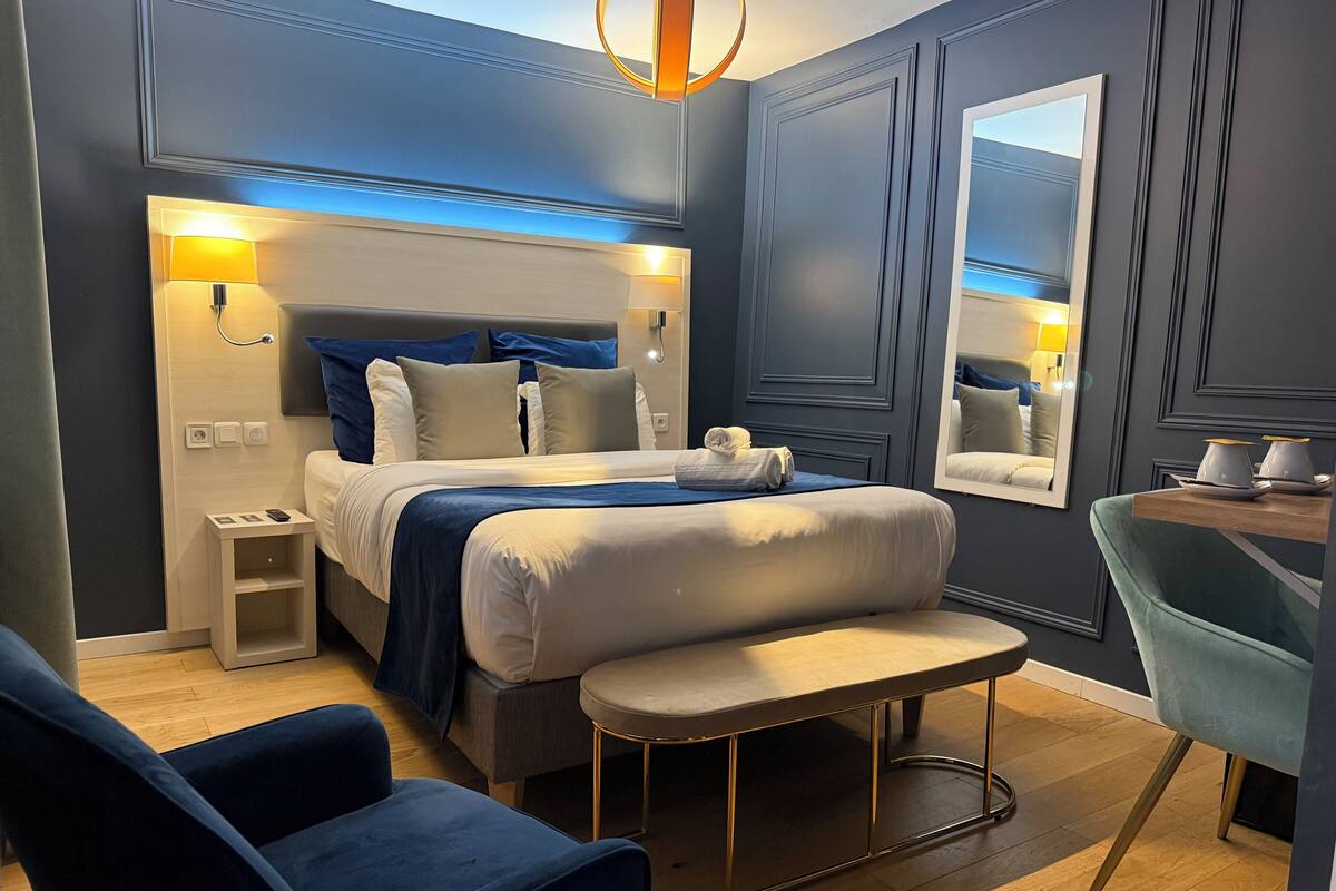 A modern hotel room with a large bed, bedside lamps, a small table, a chair, and a mirror.