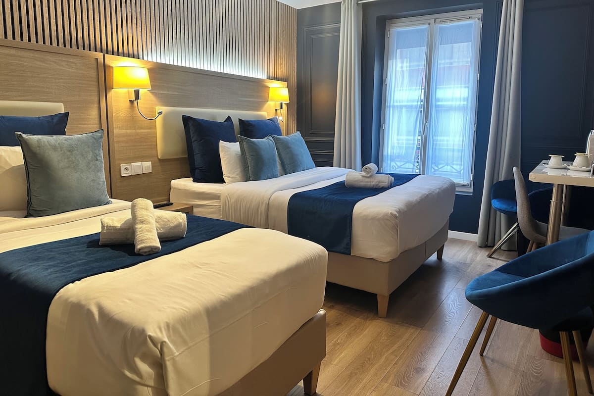 A hotel room with two beds, a dining area, and a window with curtains.