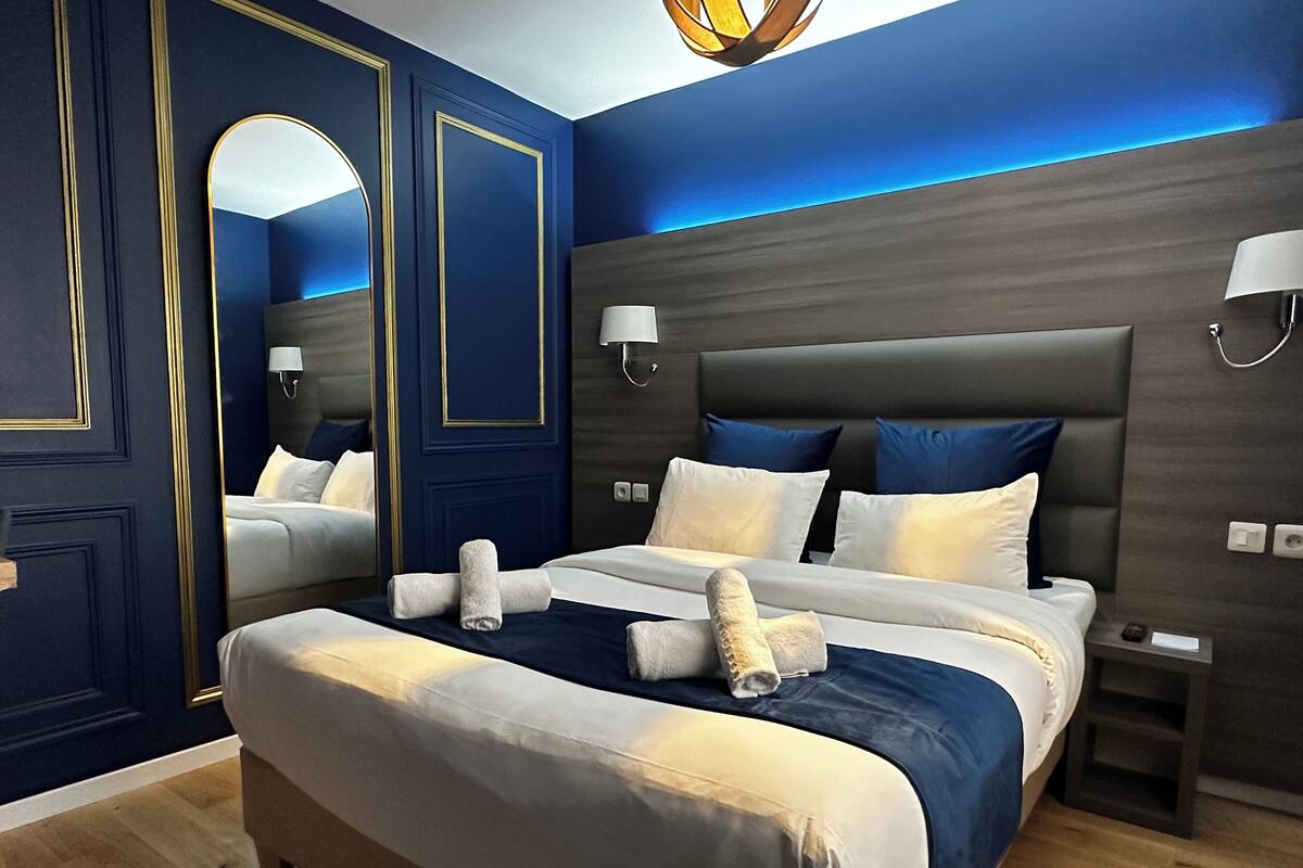 A modern bedroom with a large bed, dark blue walls, and a wooden headboard.