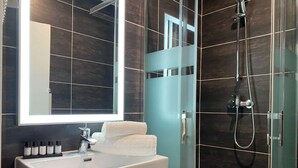 A modern bathroom with a large mirror, a white sink, a shower with a glass enclosure, and a wooden vanity.