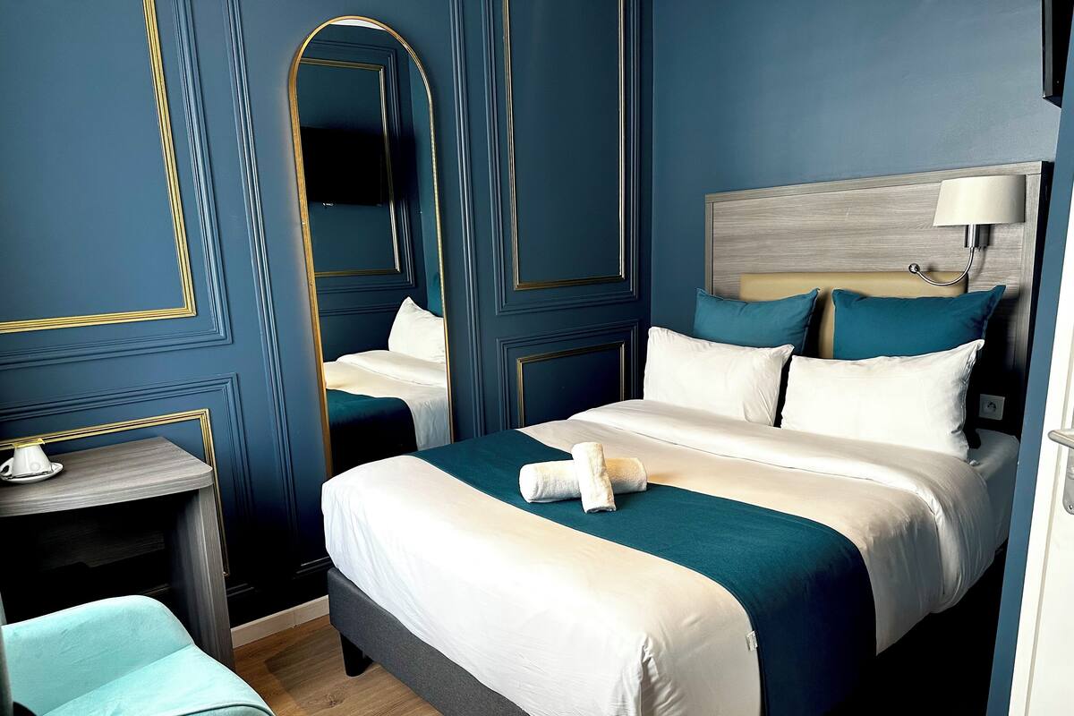 A hotel room with a large bed, a bedside table, a chair, and a mirror.