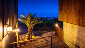 A staircase with a railing, a palm tree, and a view of a distant town at dusk. - IRO Jeju (Seogwipo)