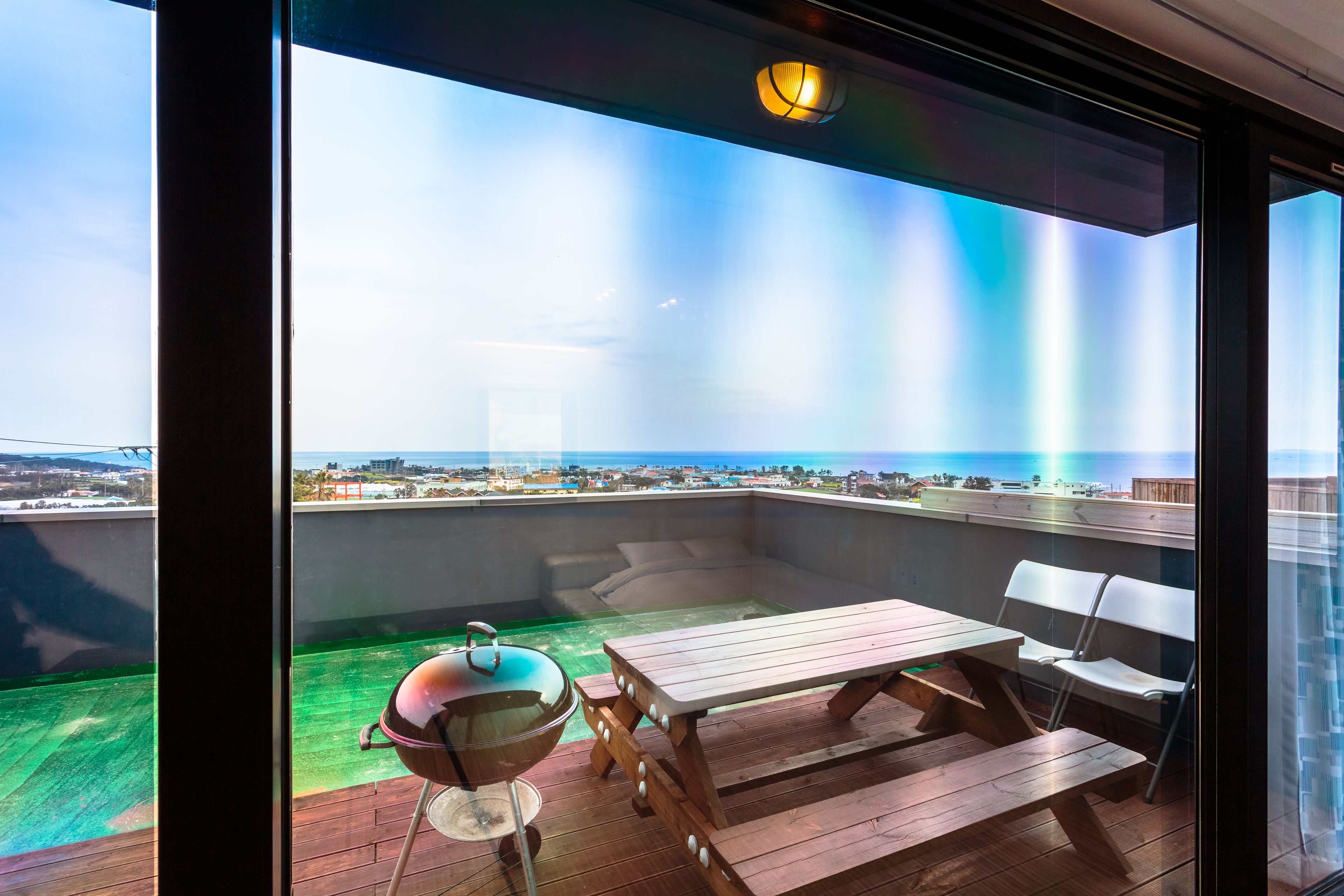 A balcony with a wooden table, chairs, and a grill.