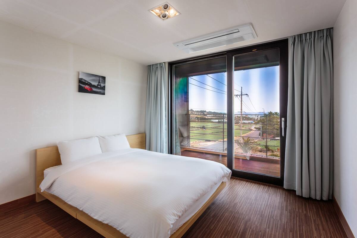A modern hotel room with a large bed, a view of the outdoors, and a ceiling-mounted air conditioner.