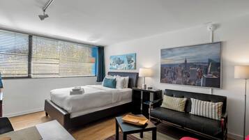 Quarto de hotel moderno com uma cama grande, um sofá, uma escrivaninha e uma pintura de paisagem urbana.