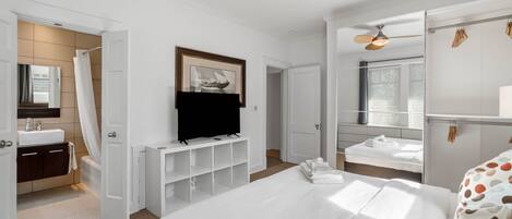 Quarto de hotel com uma cama grande, televisão, banheiro com banheira e ventilador de teto.