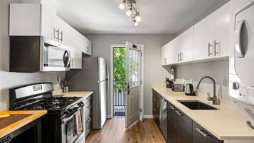 A modern kitchen with stainless steel appliances, white cabinetry, and a large window.