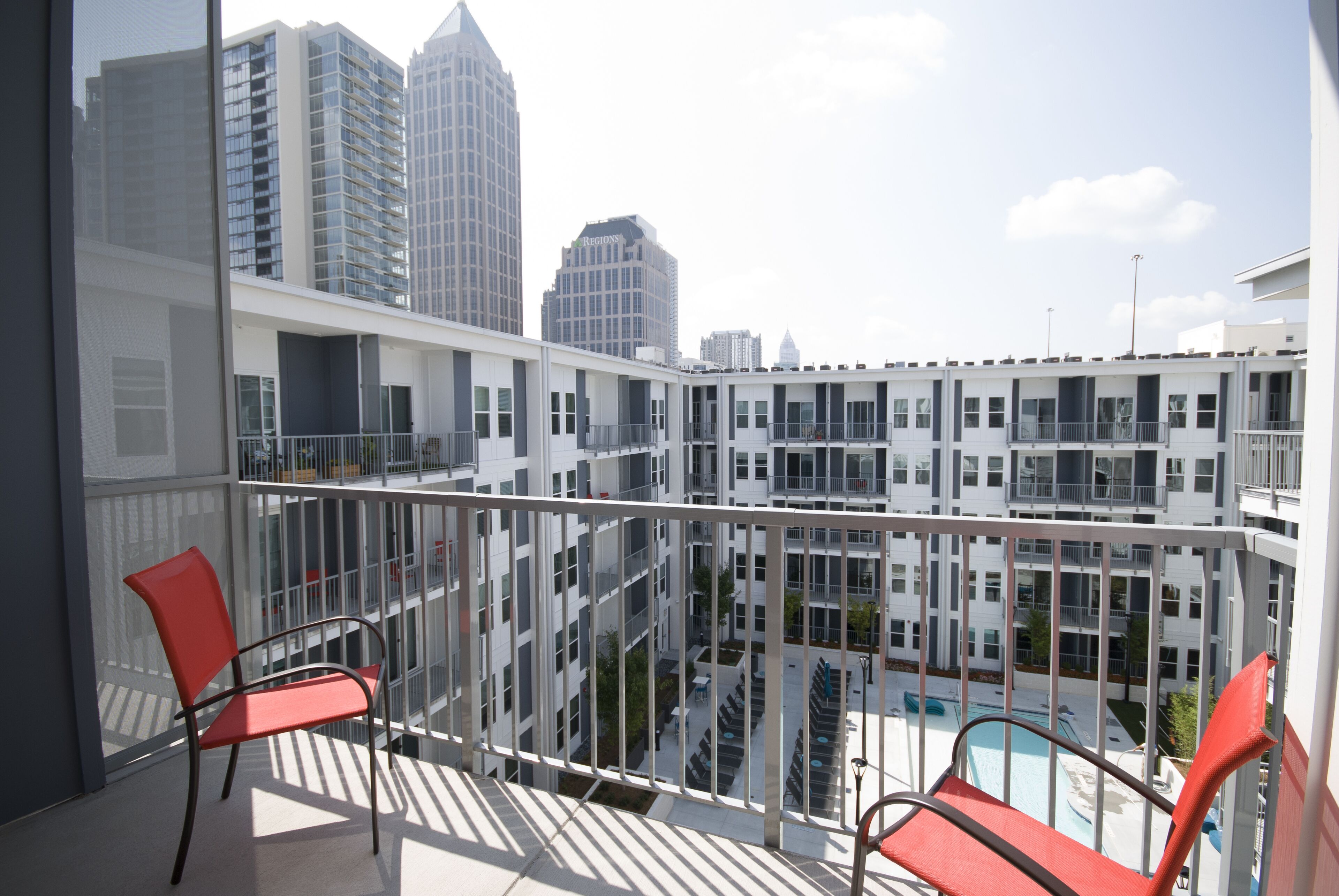 A balcony with two red chairs, a pool, and high-rise buildings in the background.