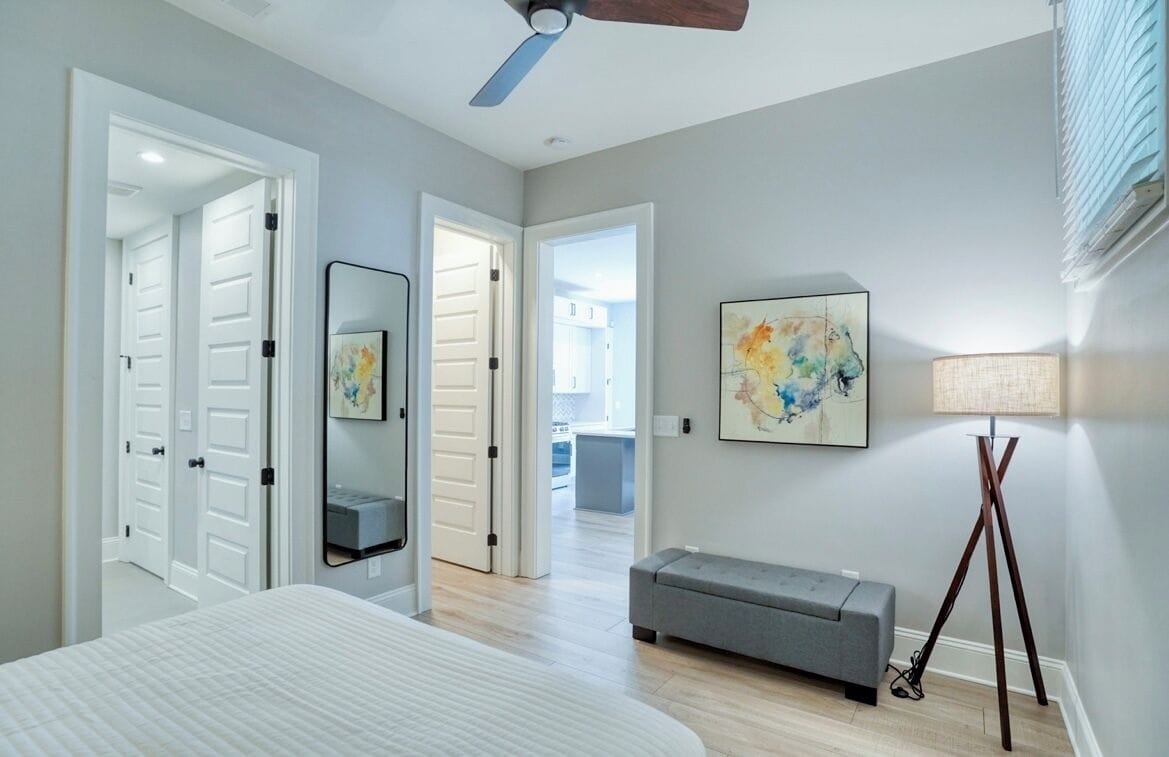 A bedroom with a bed, a gray bench, a floor lamp, and a ceiling fan.