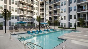 Un hotel moderno con piscina, varios balcones y sillones de descanso.