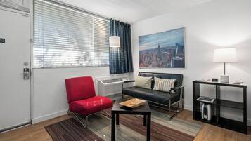 A modern hotel room with a red armchair, a black sofa, a cityscape painting, a lamp, and a small table with a tray.