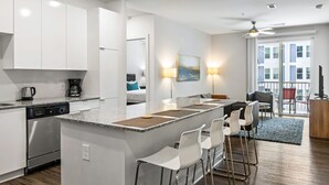 Una cocina moderna con armarios blancos, lavavajillas y una zona de bar con sillas blancas.