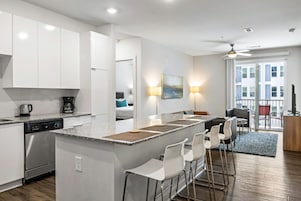 Una cocina moderna con armarios blancos, lavavajillas y una zona de bar con sillas blancas.