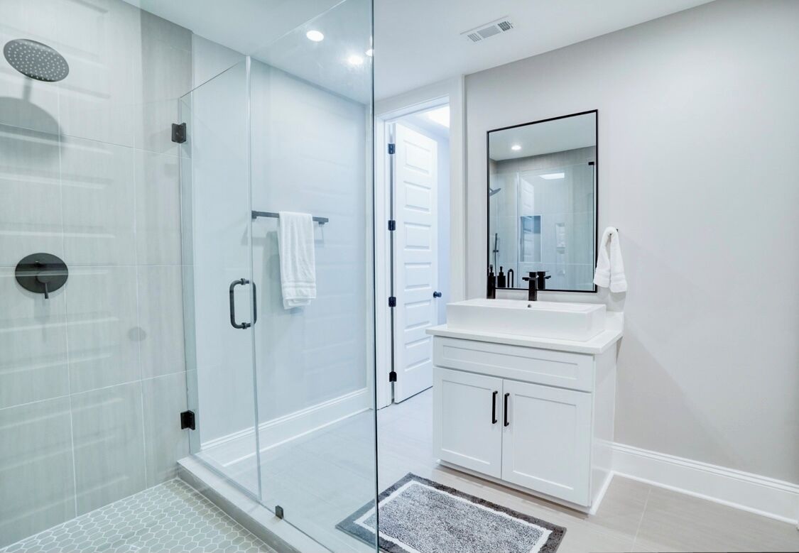 A modern bathroom with a glass shower enclosure, a white vanity with a mirror, and a tiled floor.