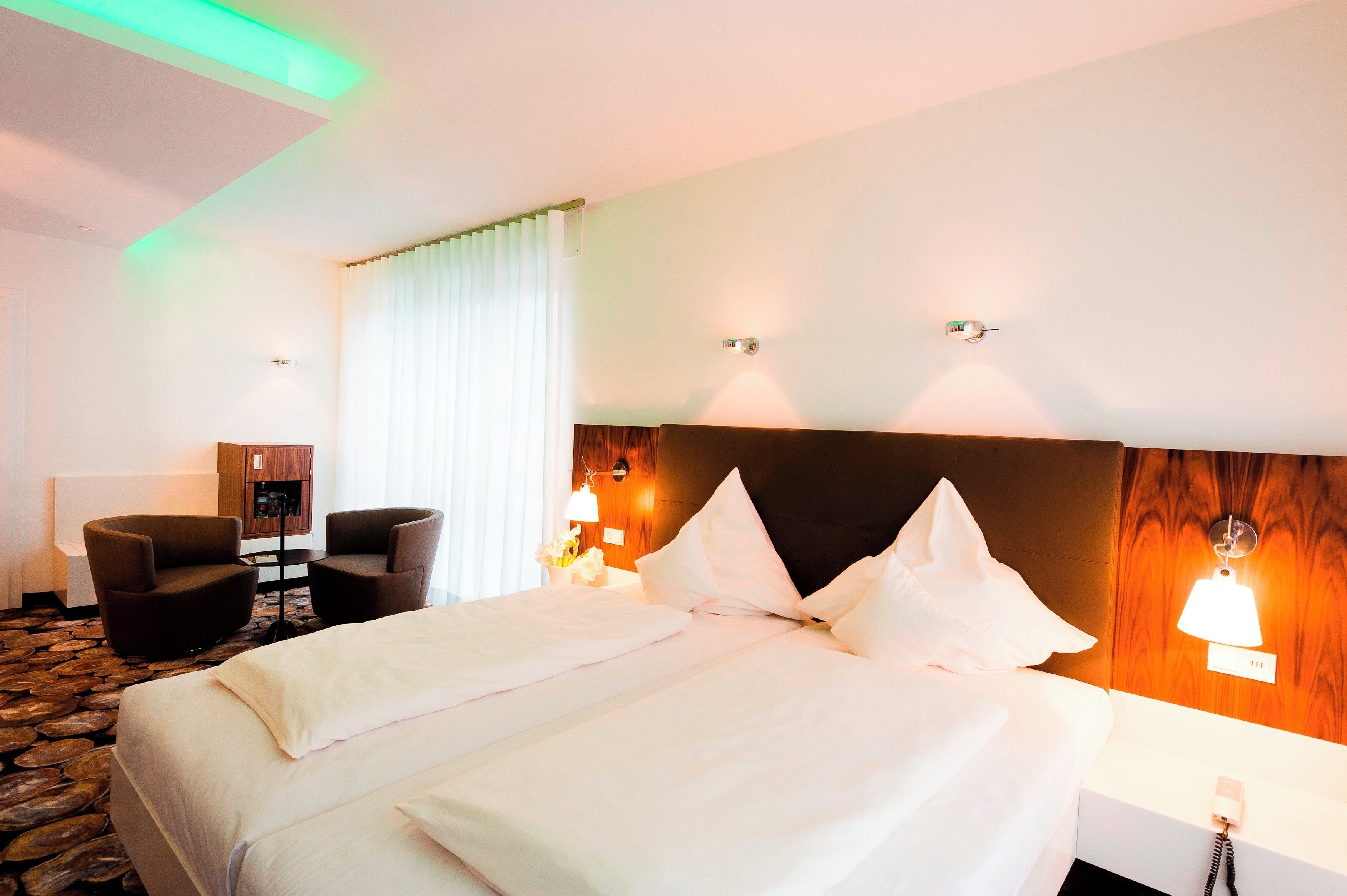 Habitación de hotel con una cama grande, dos sillones, un escritorio y un mini bar.