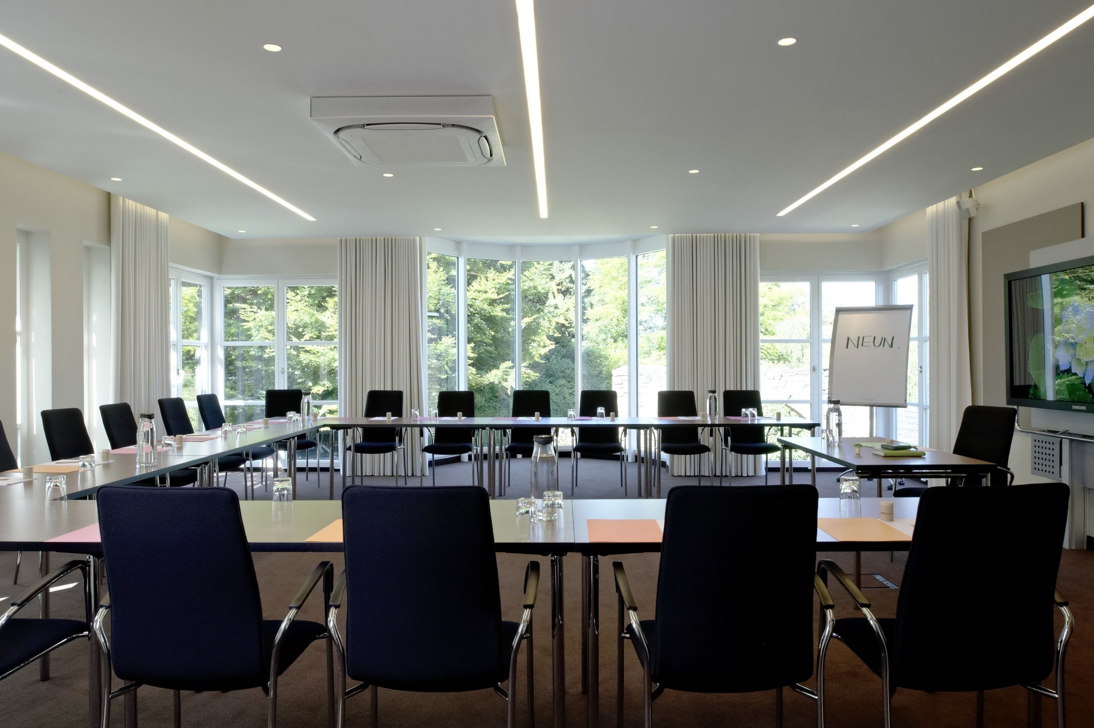 Una sala conferenze con un lungo tavolo, sedie nere e una lavagna.