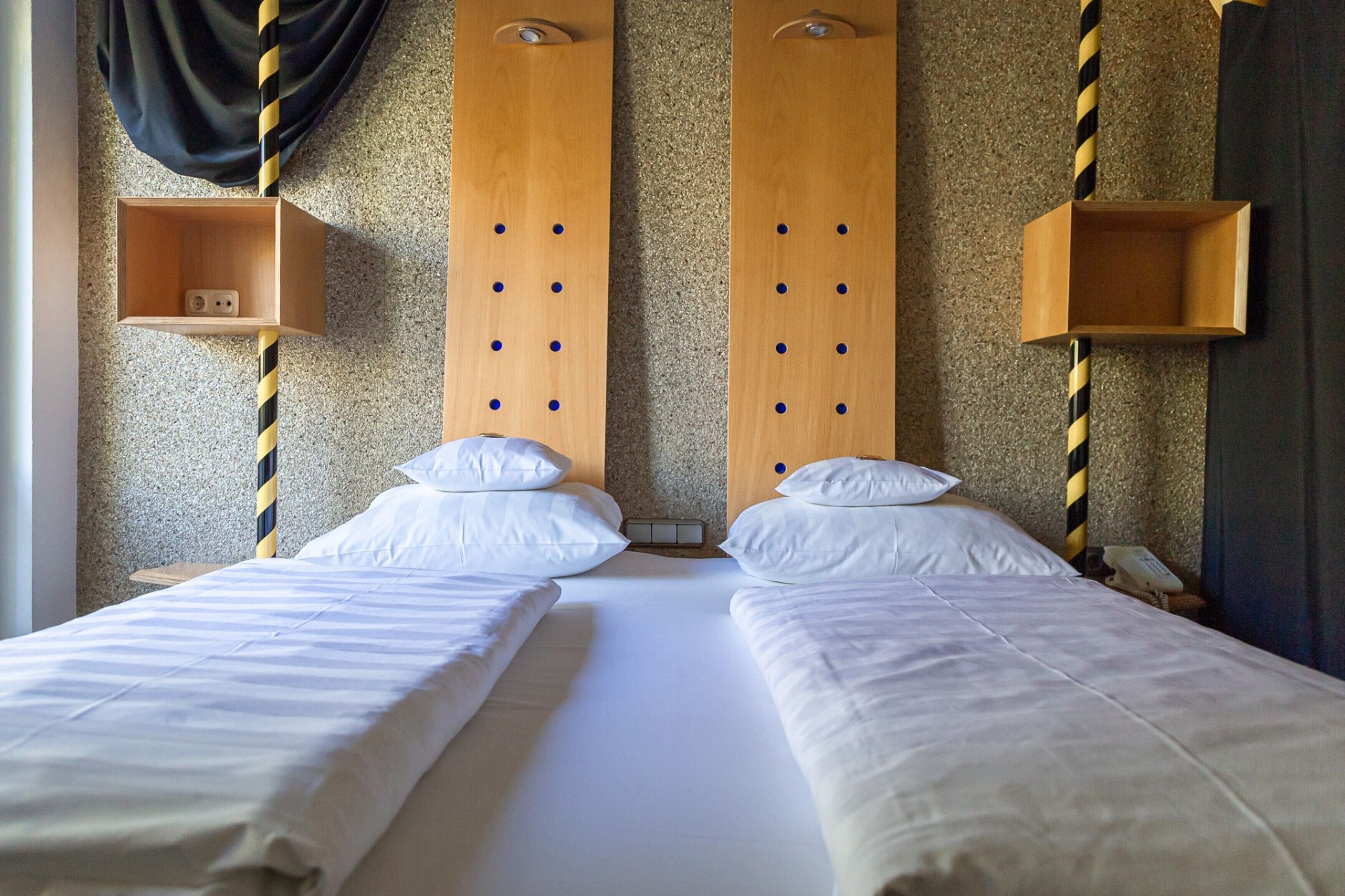 A hotel room with two beds, wooden headboards, and striped poles.