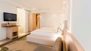 Habitació d'hotel moderna amb llit, televisió, taula de nit i zona de seients petita.