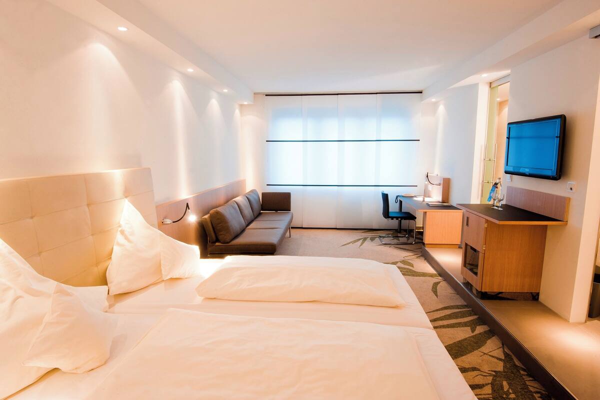 A hotel room with a bed, a sofa, a desk, and a TV.