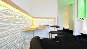 Un espace d’attente moderne avec un mur incurvé, un comptoir d’accueil et une porte illuminée de lumière verte.