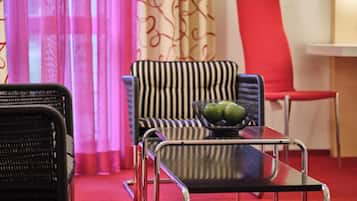 Una habitación con un sofá a rayas, un sillón de mimbre negro, una mesa de vidrio con estructura metálica y una silla roja.