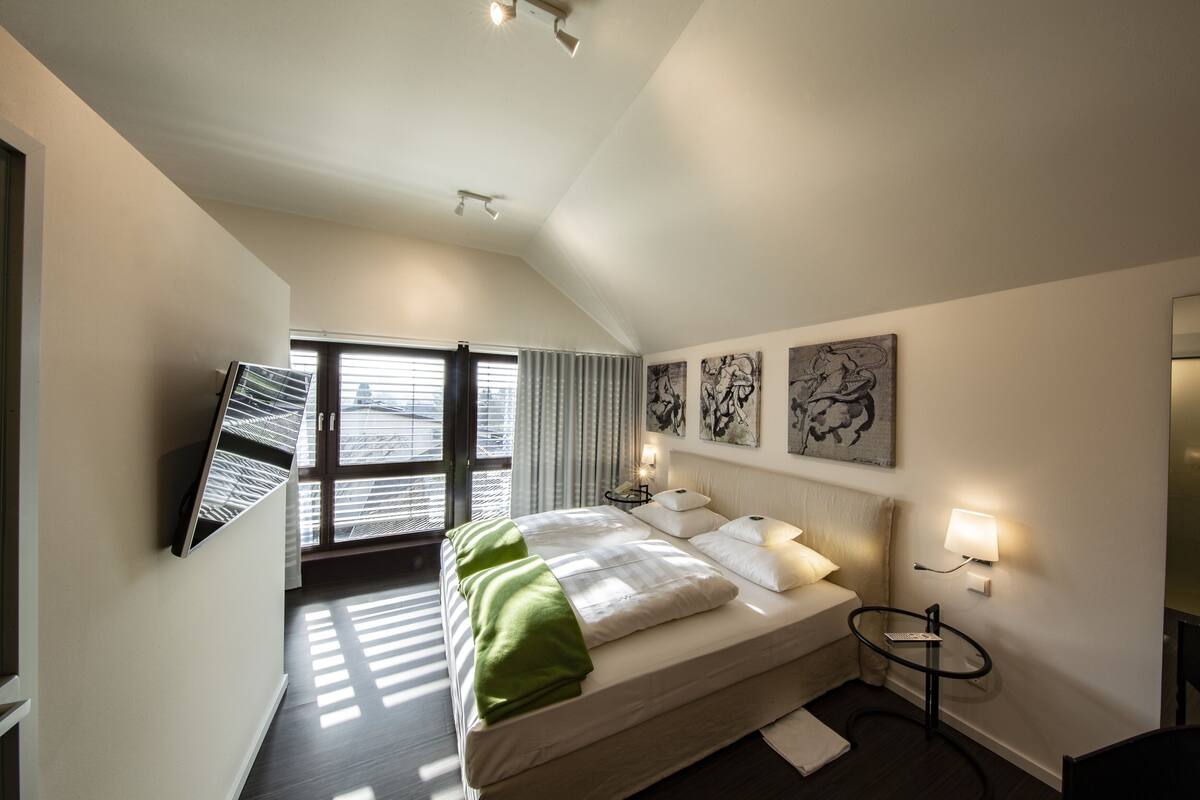 A modern hotel room with a bed, bedside lamps, a small table, and artwork on the walls.