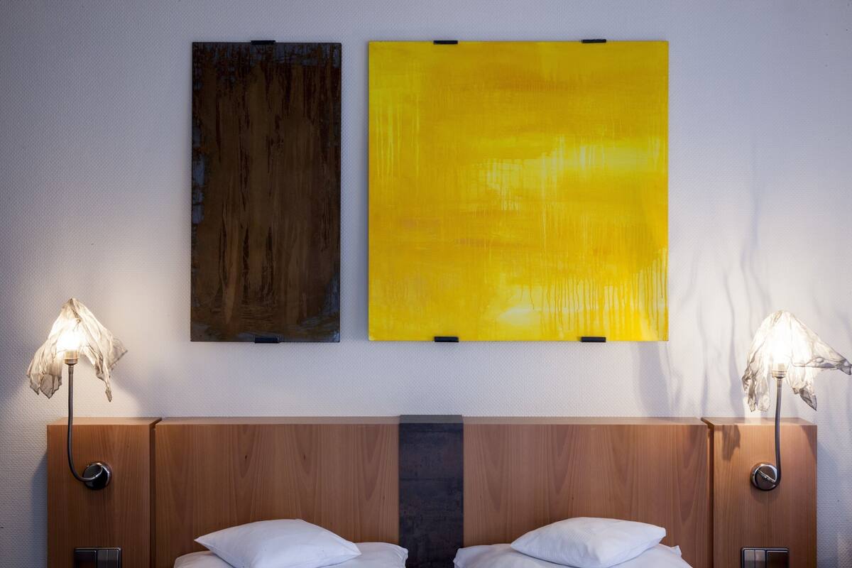 Una habitación de hotel con cabecera de madera, dos camas con sábanas blancas y dos lámparas fijadas a la pared.