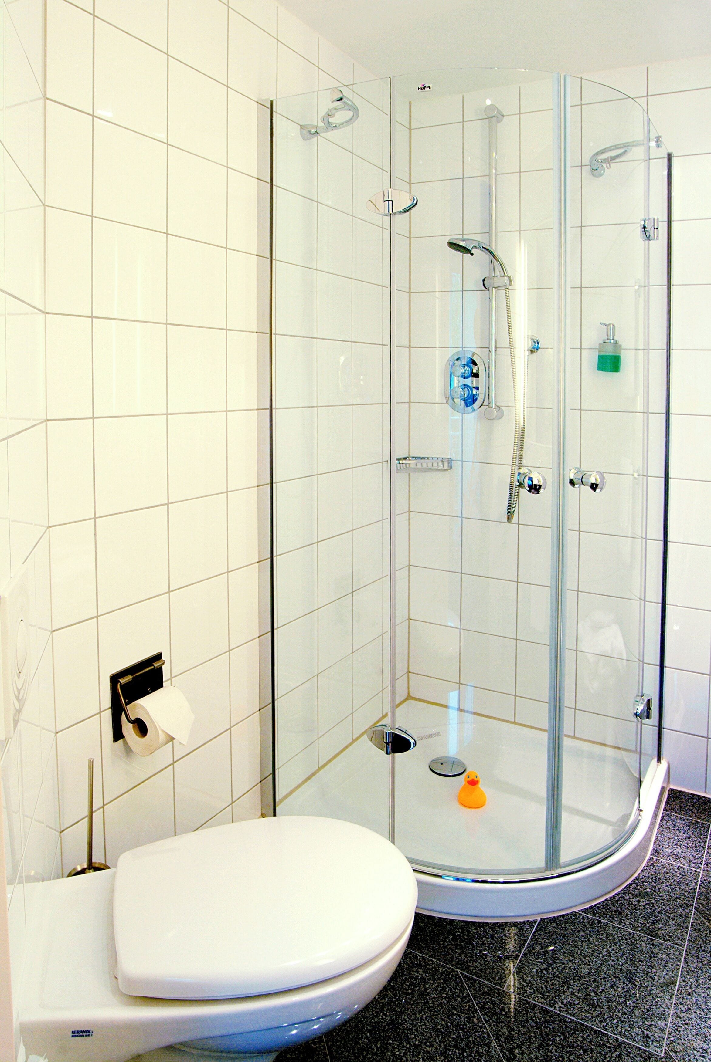 A glass-enclosed shower stall with a handheld showerhead and a handheld faucet.