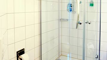 A glass-enclosed shower stall with a handheld showerhead and a handheld faucet.