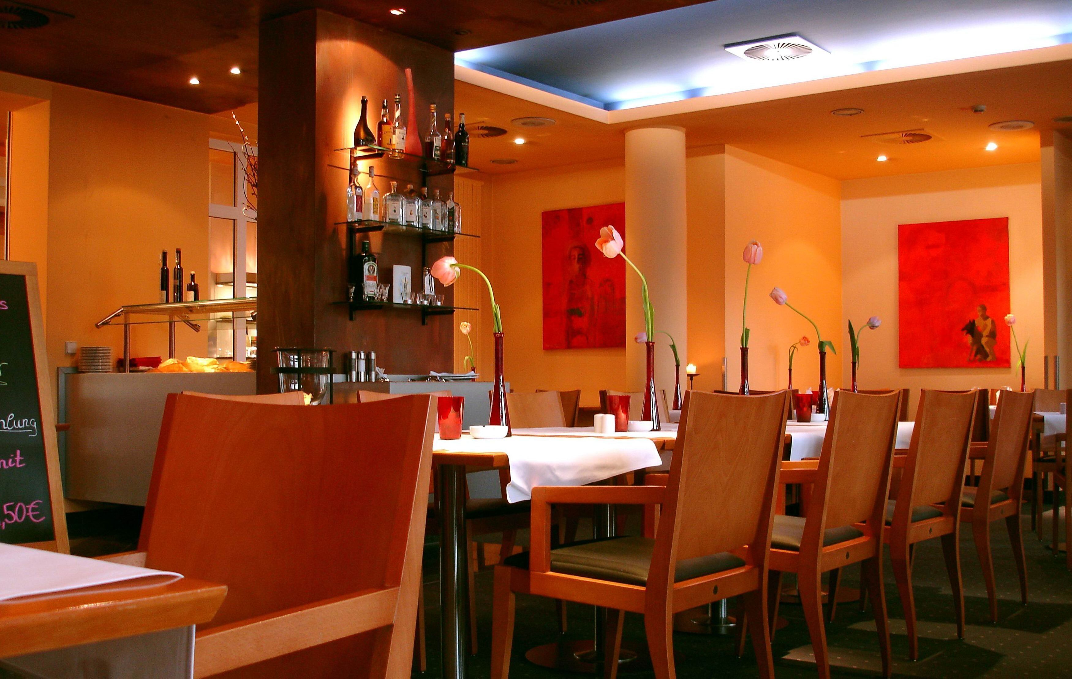 A restaurant interior with wooden chairs, tables, and red floral wall art.