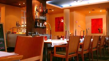 A restaurant interior with wooden chairs, tables, and red floral wall art.