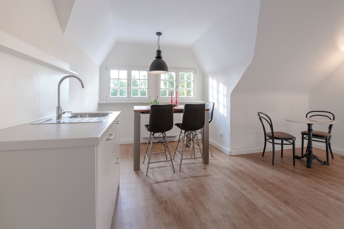 Una cocina moderna con encimera blanca, pileta y zona de comedor con dos sillas y una mesa.