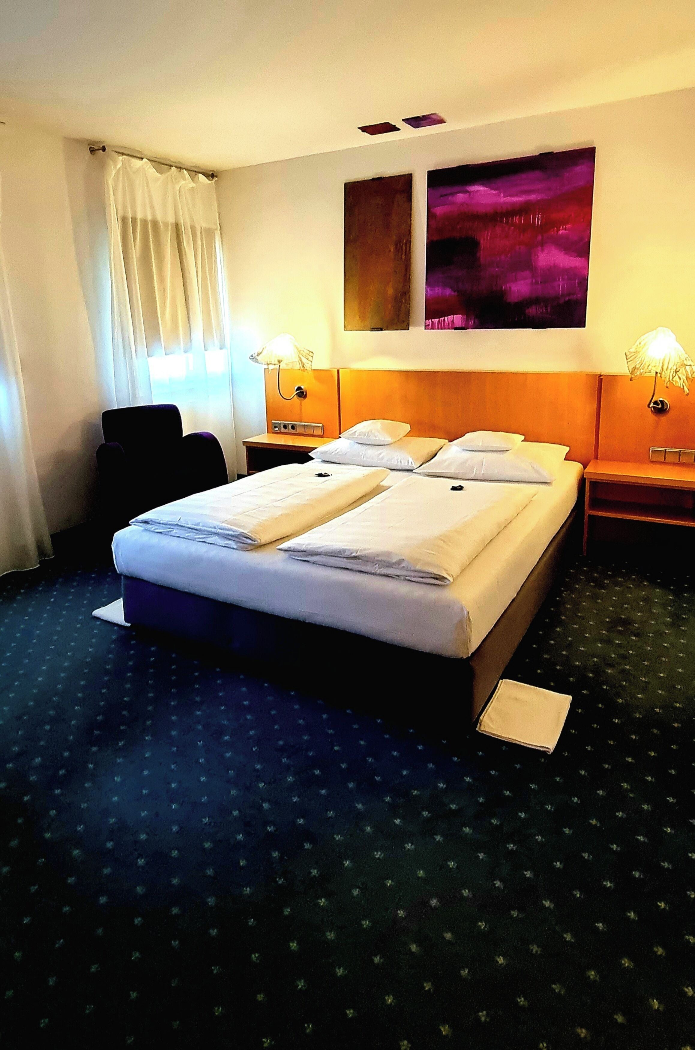 A hotel room with a large bed, two bedside tables, a chair, and a window with curtains.
