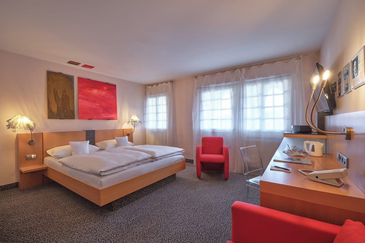 Una habitación de hotel con una cama grande, un escritorio con teléfono, una silla roja y una cafetera.