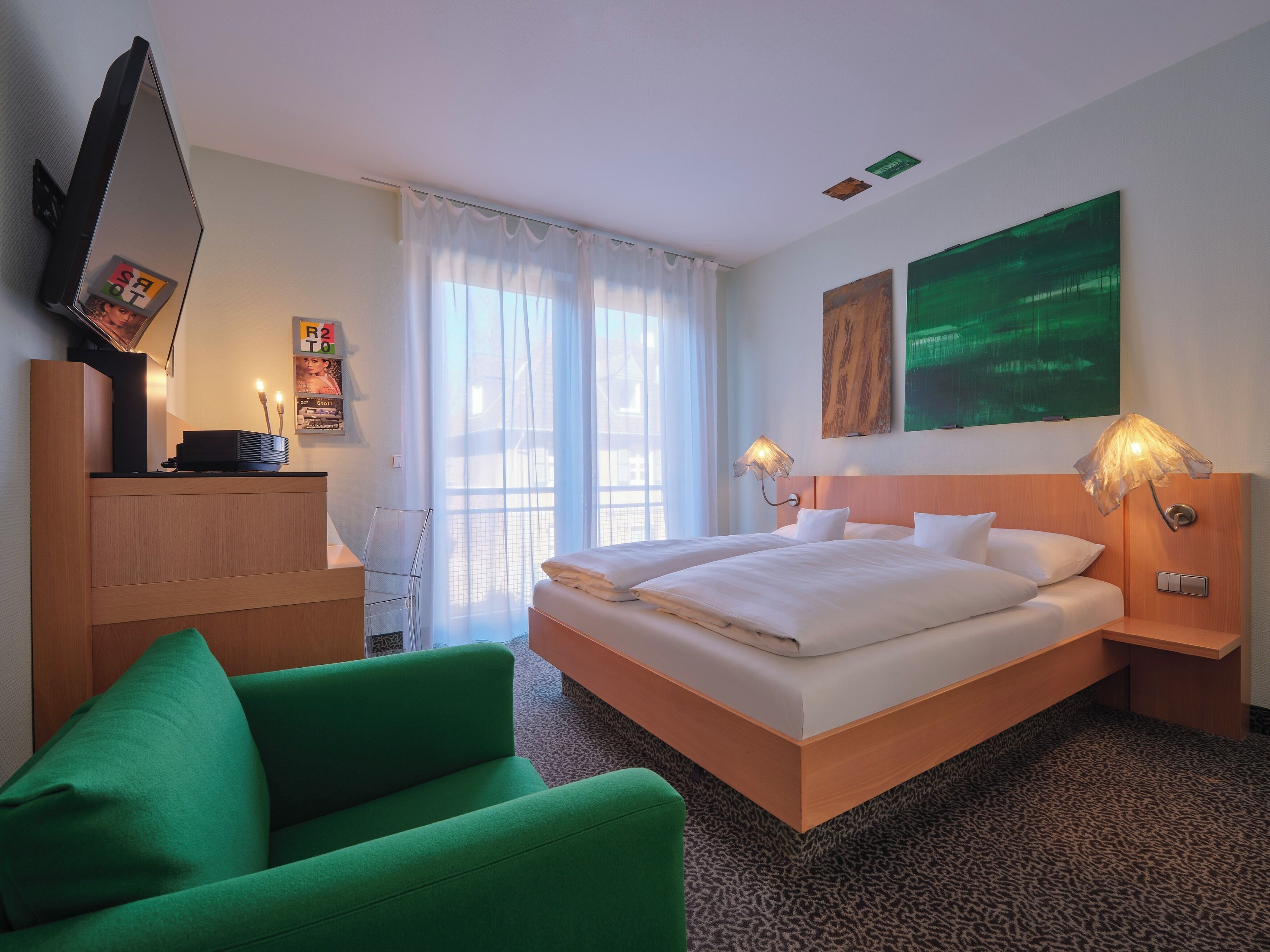 Habitación de hotel con una cama grande, un escritorio, una silla, un televisor y obras de arte en las paredes.