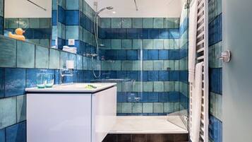 Een moderne badkamer met blauwe wandtegels, een witte wastafel en een douchehoek.