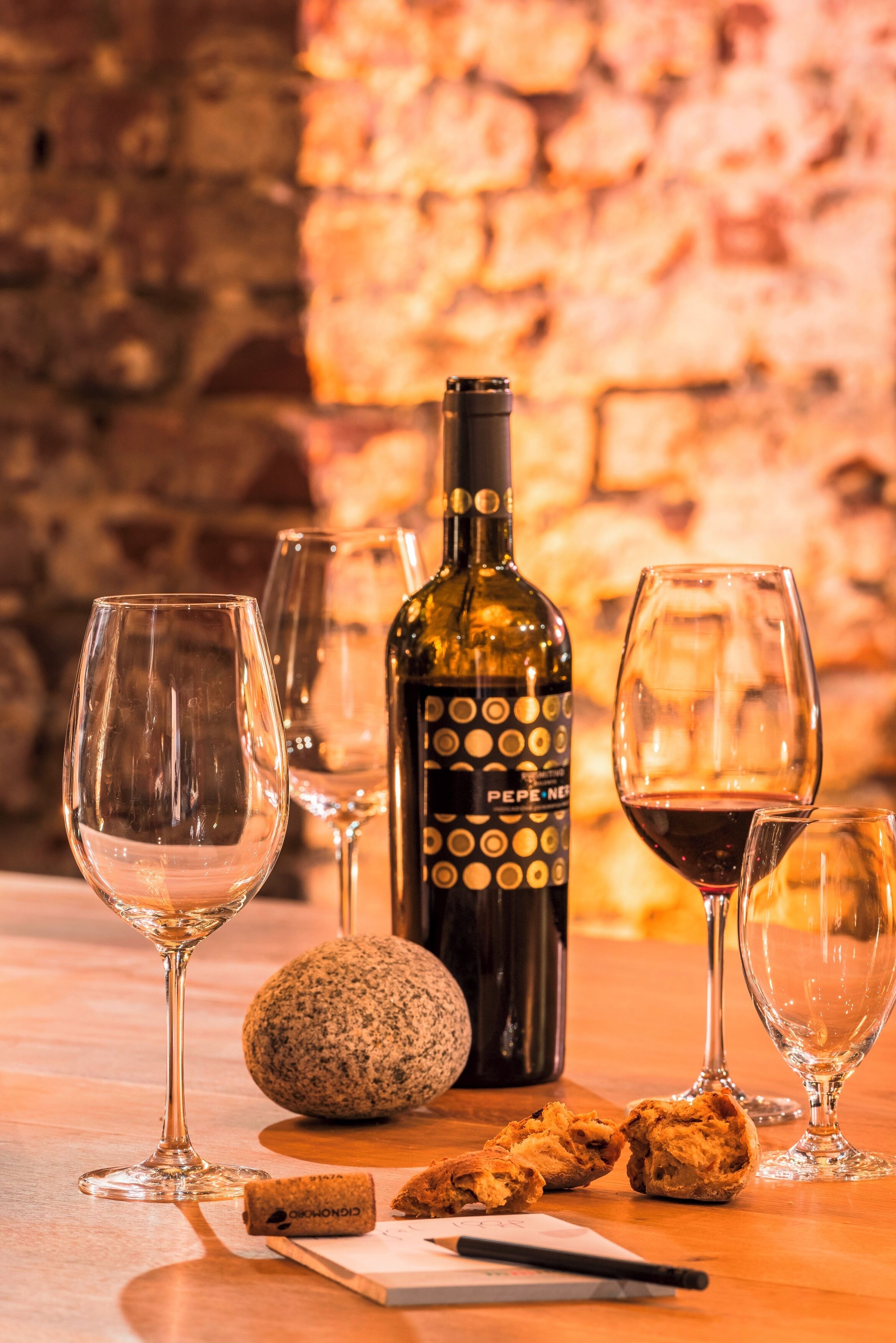 Una botella de vino, dos copas, un corcho y un papel sobre una mesa de madera.