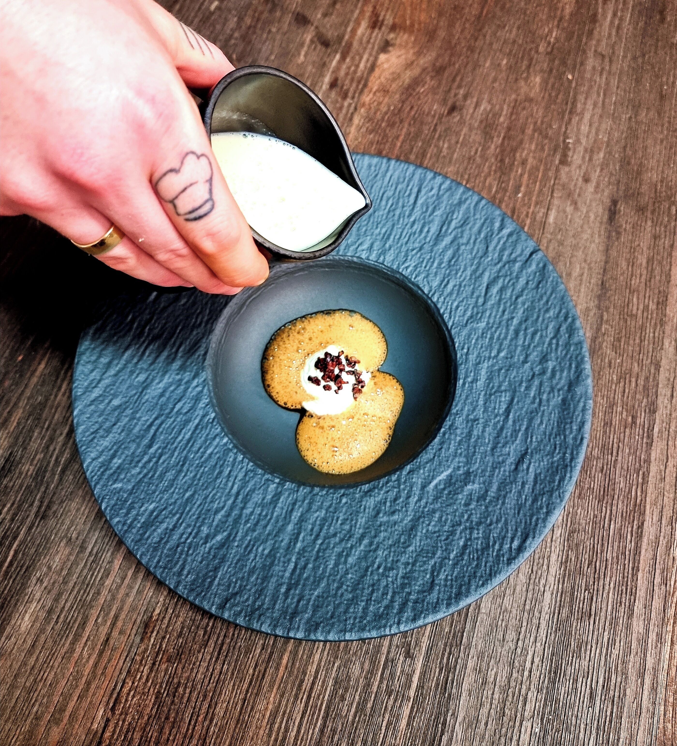 A hand pouring cream into a bowl with cookies on a blue mat.