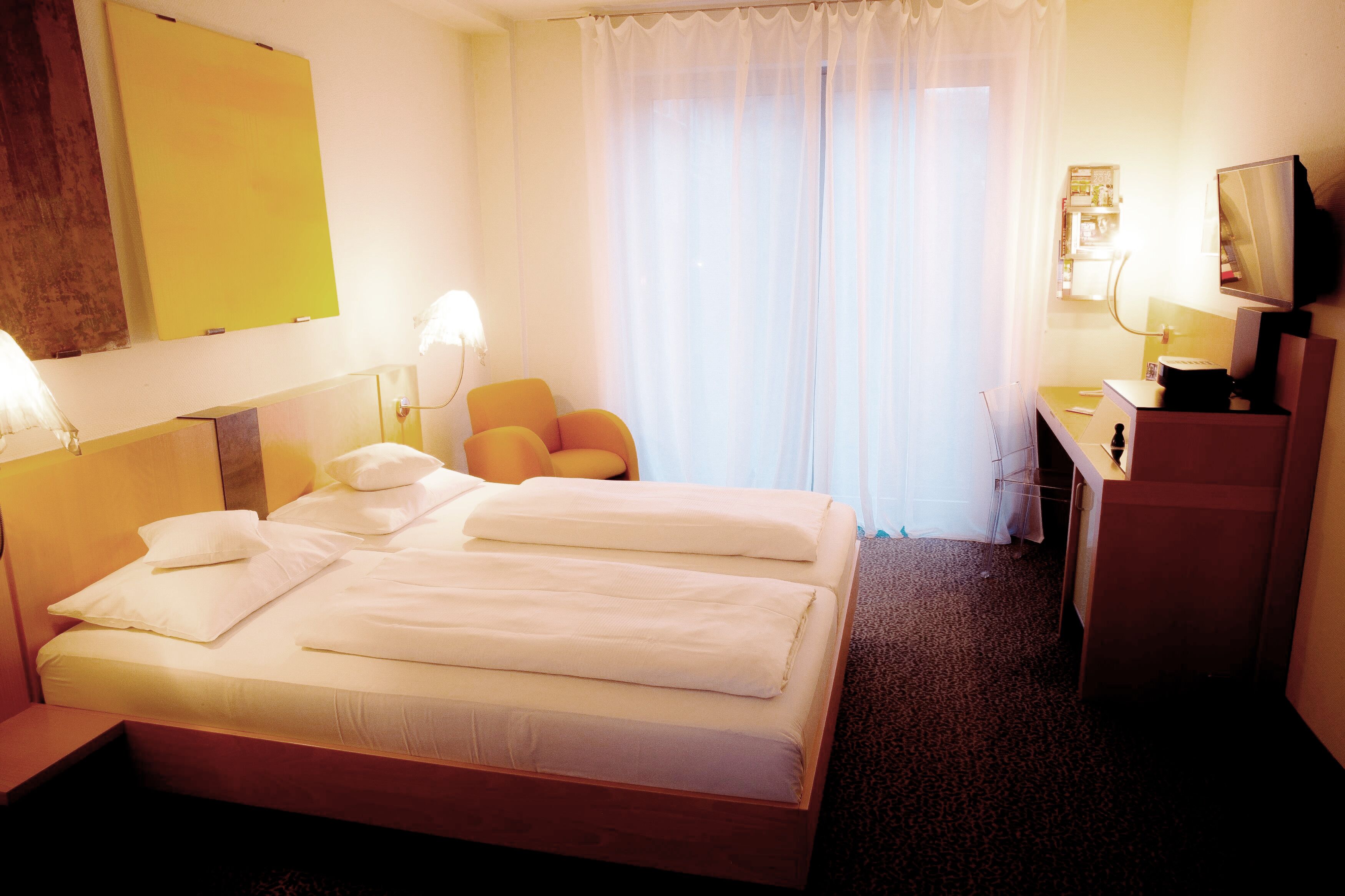 Habitación de hotel con una cama grande, un escritorio con silla, televisión y ventana con cortinas.