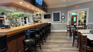 Eine Bar mit einer langen Theke, mehreren Barhocker und einer Auswahl an Flaschen und Gläsern.