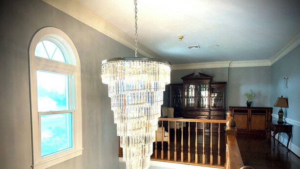 Ein geräumiger Raum mit einem großen Chandelier, einer Holztreppe und Blick durch ein Rundbogenfenster.
