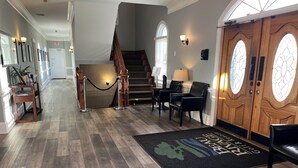 Eine Hotelhalle mit Holzboden, einem Empfangstresen, einer Treppe und einer Rezeption mit zwei Stühlen und einer Lampe.